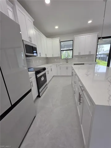 Kitchen with electric stove, stainless steel microwave, hanging light fixtures, freestanding refrigerator, and white cabinets