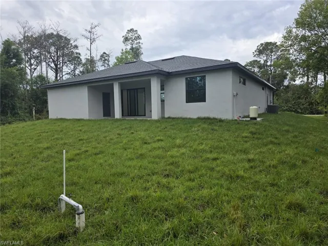 Back of house with a yard, roof with shingles, stucco siding, and central air condition unit