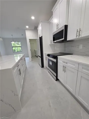 Kitchen with freestanding refrigerator, white cabinets, stainless steel microwave, and black / electric stove