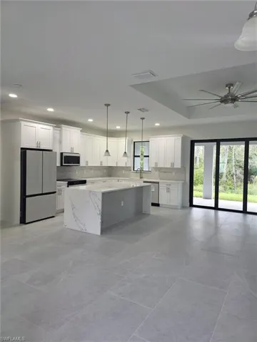 Kitchen featuring appliances with stainless steel finishes, open floor plan, a center island, decorative light fixtures, and white cabinetry