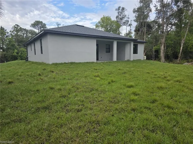 Back of property featuring stucco siding, a shingled roof, and a yard