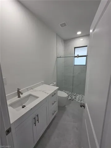 Full bath featuring toilet, a marble finish shower, visible vents, and vanity