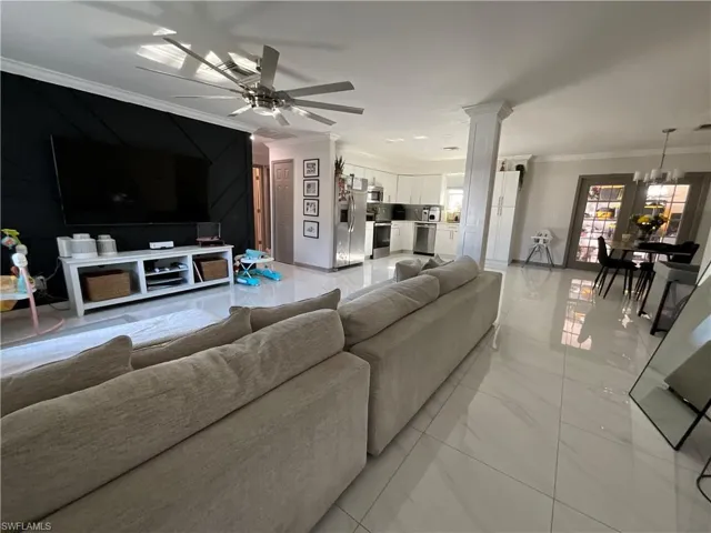 Living room with crown molding, ceiling fan, light marble finish floors, and a chandelier