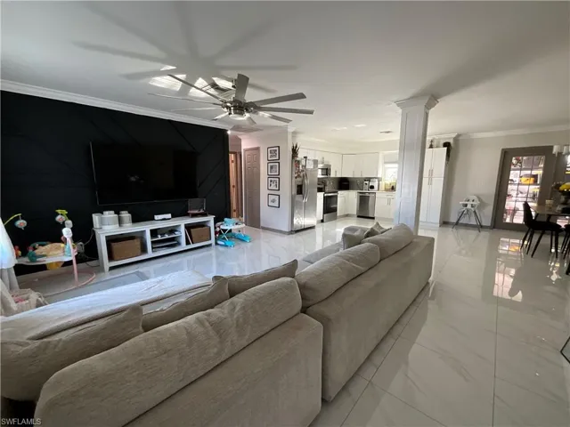 Living room featuring crown molding, light marble finish floors, a ceiling fan, and ornate columns