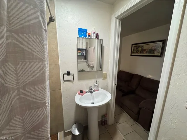 Bathroom featuring a textured wall, curtained shower, and light tile patterned floors