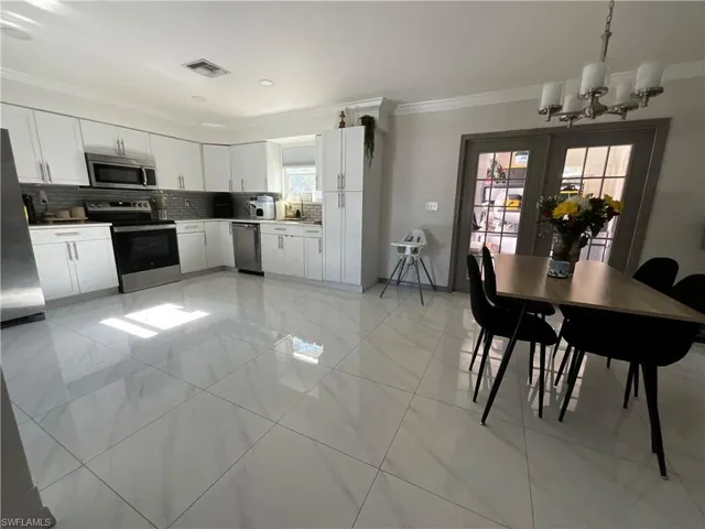 Kitchen with stainless steel appliances, backsplash, white cabinetry, ornamental molding, and a chandelier