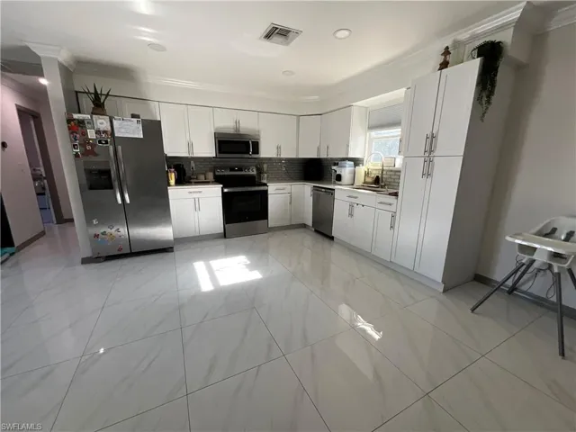 Kitchen featuring crown molding, stainless steel appliances, white cabinetry, and backsplash