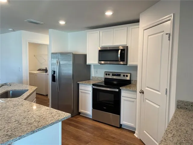 Kitchen featuring white cabinets, light stone counters, sink, and appliances with stainless steel finishes