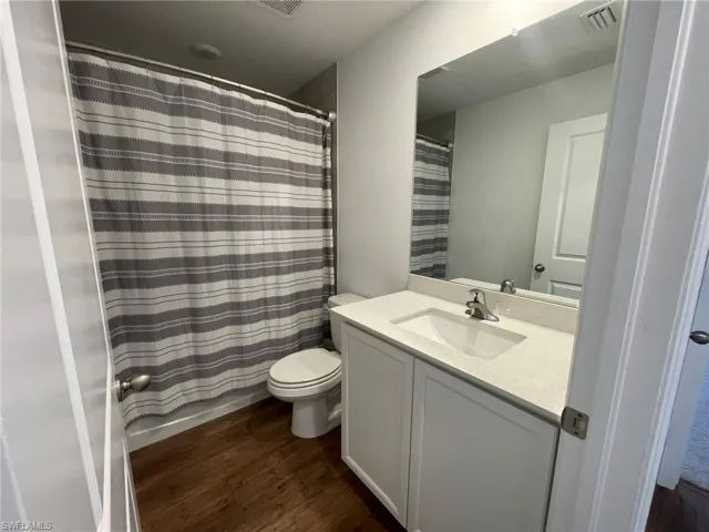Full bathroom featuring hardwood / wood-style floors, vanity, shower / tub combo, and toilet