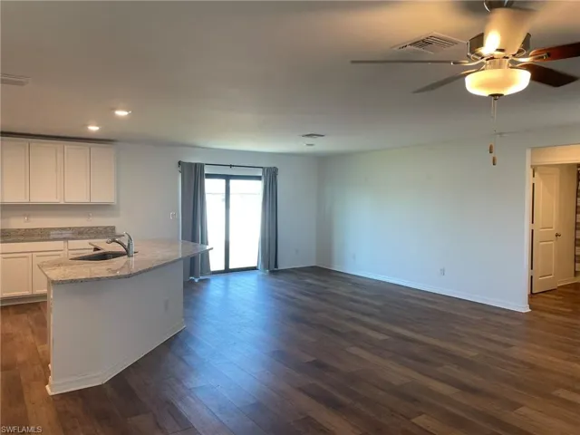 Kitchen featuring light stone countertops, sink, dark hardwood / wood-style flooring, an island with sink, and white cabinets