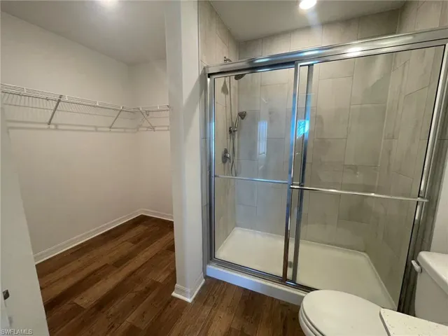 Bathroom with wood-type flooring, a shower with shower door, and toilet
