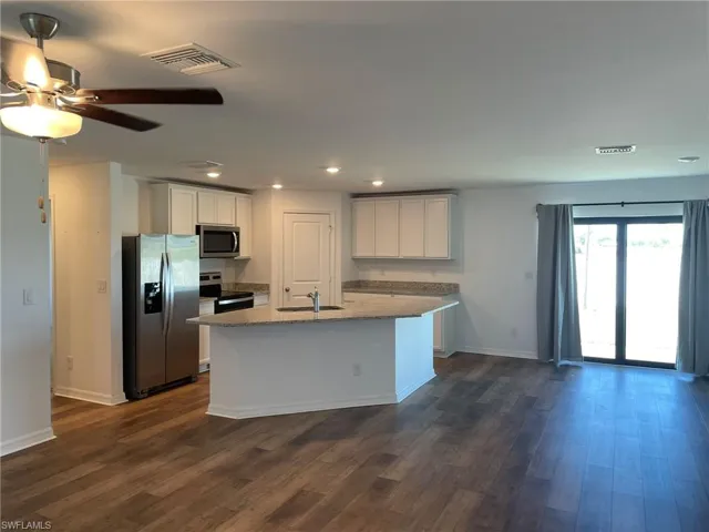 Kitchen featuring white cabinetry, sink, dark hardwood / wood-style floors, a center island with sink, and appliances with stainless steel finishes