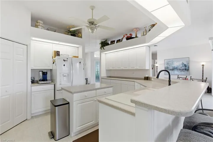 Kitchen with a center island, a peninsula, white fridge with ice dispenser, light quartz countertops, and a breakfast bar