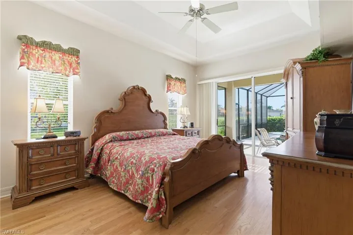 Primary Bedroom featuring a tray ceiling, access to outside, light wood finished floors, ceiling fan, and multiple windows