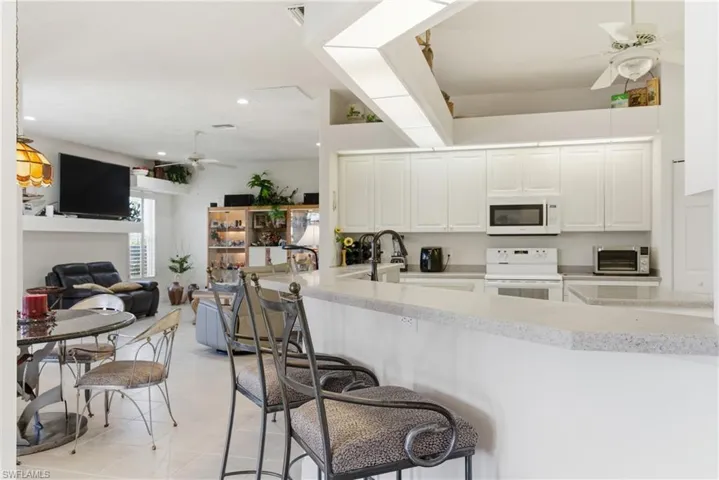 Kitchen featuring ceiling fan, white appliances, white cabinetry, a kitchen breakfast bar, and open floor plan