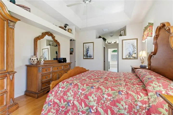 Bedroom with a raised ceiling, light wood finished floors, and a ceiling fan