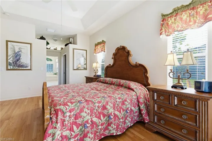 Bedroom featuring light wood-style floors, multiple windows, and a tray ceiling
