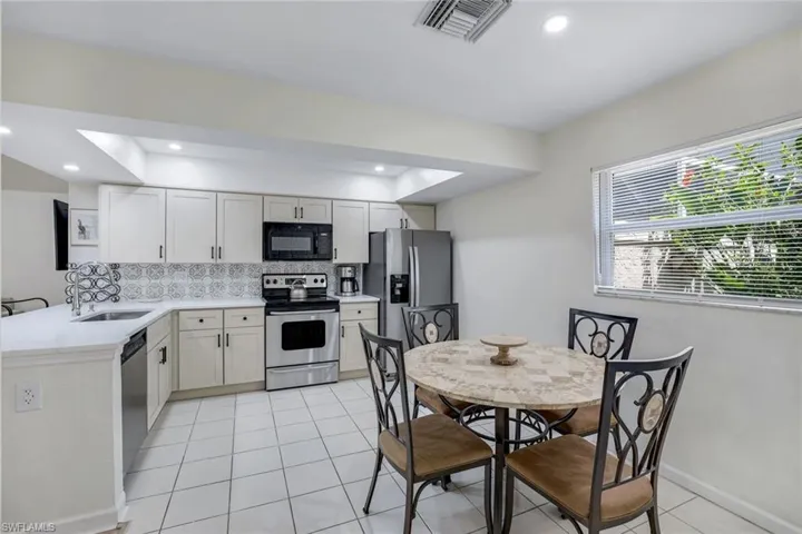 Kitchen with a sink, backsplash, appliances with stainless steel finishes, light countertops, and light tile patterned floors