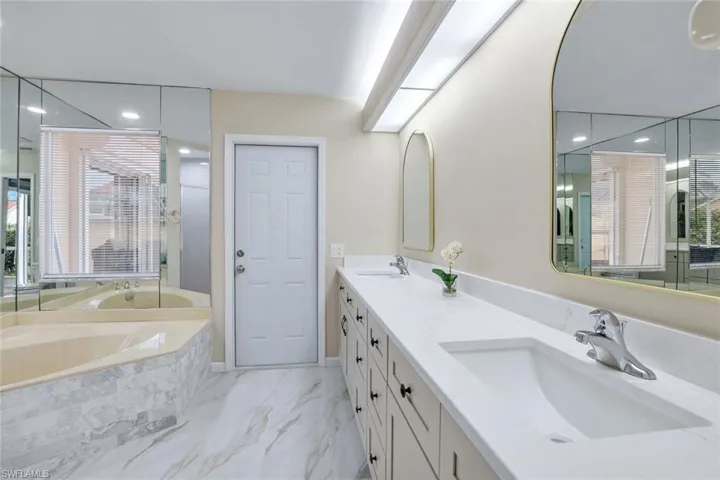 Full bathroom featuring double vanity, a garden tub, marble finish floor, and a sink
