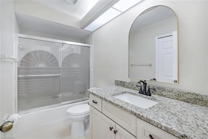 Full bath featuring shower / bath combination with glass door, toilet, vanity, and tile patterned floors