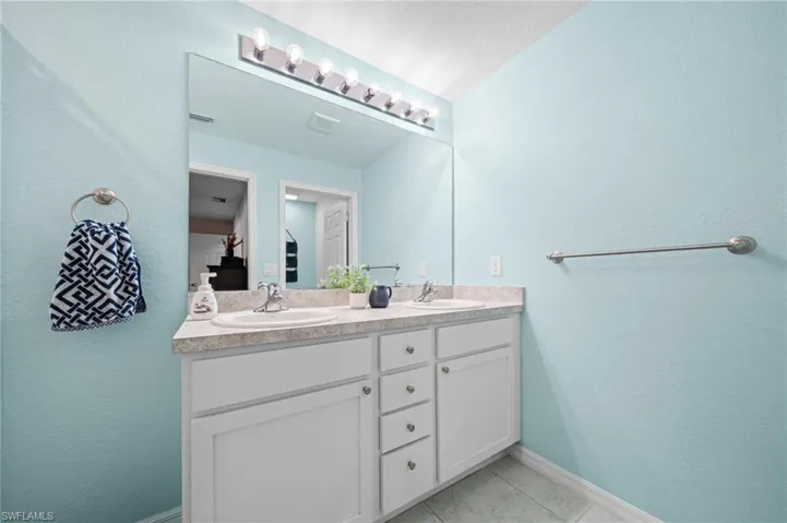 Bathroom featuring a textured wall, double vanity, and light tile patterned flooring