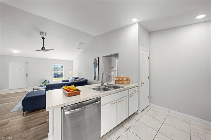 Kitchen featuring stainless steel dishwasher, light countertops, lofted ceiling, white cabinetry, and open floor plan