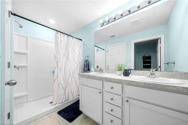 Bathroom featuring a shower stall, light tile patterned floors, and double vanity
