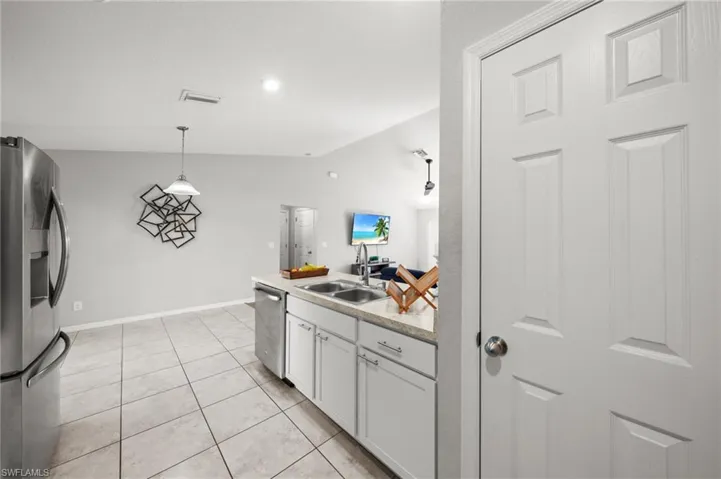 Kitchen with appliances with stainless steel finishes, hanging light fixtures, white cabinetry, vaulted ceiling, and light tile patterned floors
