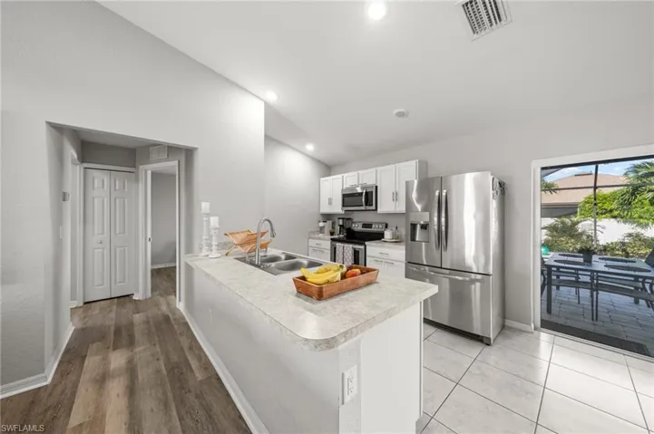 Kitchen with stainless steel appliances, light countertops, white cabinets, a peninsula, and vaulted ceiling