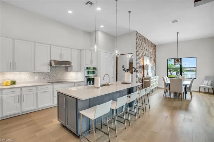 Kitchen with tasteful backsplash, light hardwood flooring, pendant lighting, and a kitchen island with sink