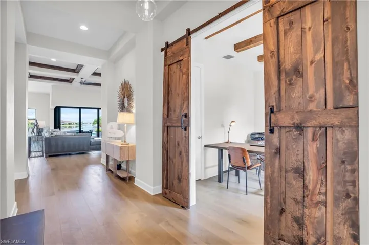 Hall featuring a barn door to the den, coffered ceiling, beamed ceiling, and light hardwood flooring