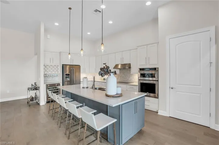 Kitchen featuring backsplash, a center island with sink, light hardwood flooring, appliances with stainless steel finishes, and pendant lighting
