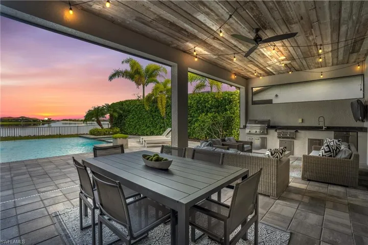 Patio terrace at dusk featuring an outdoor kitchen, area for grilling, ceiling fan, and a fenced in pool