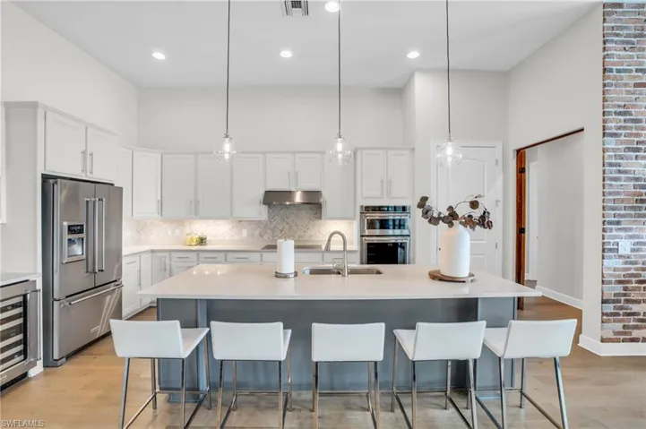 Kitchen with a center island with sink, light hardwood flooring, tasteful herringbone backsplash, and appliances with stainless steel finishes