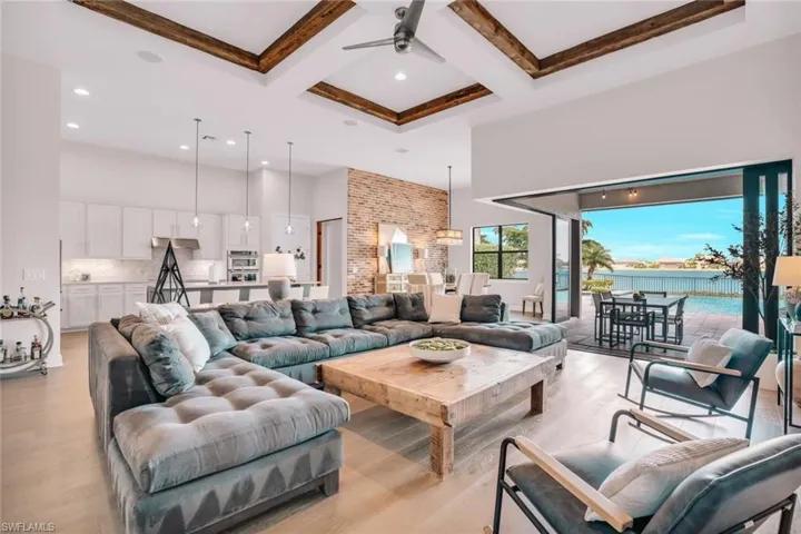 Living room with coffered ceiling, beamed ceiling, a high ceiling, ceiling fan, and light wood-type flooring