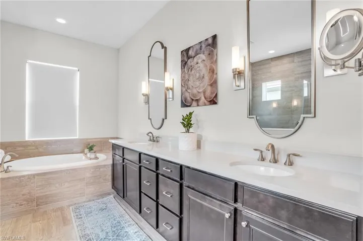 Primary bathroom with vanity with extensive cabinet space, tiled tub, and dual sinks
