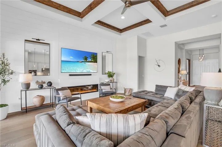 Living room with custom shiplap feature wall with Dimplex fireplace, beamed coffered ceiling, light hardwood floors, coffered ceiling, and ceiling fan