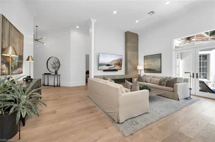 Living room with light hardwood / wood-style floors, an inviting chandelier, french doors, and ornamental molding