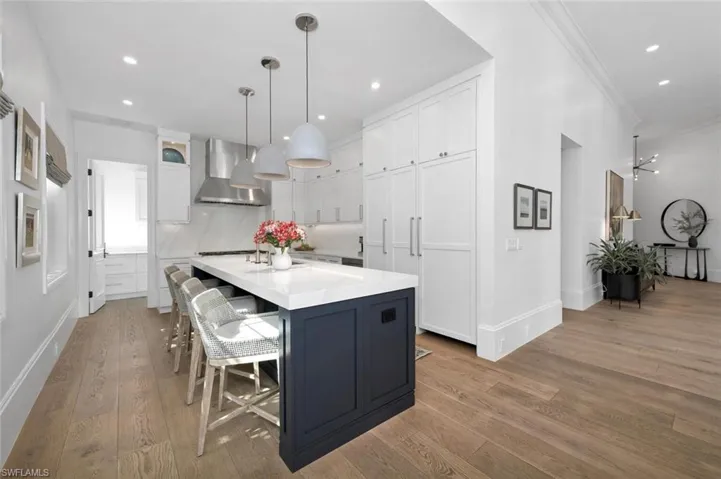 Kitchen with wall chimney range hood, decorative light fixtures, light hardwood / wood-style floors, and white cabinets