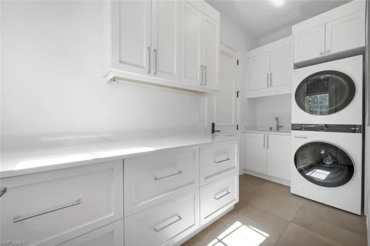 Laundry area featuring cabinets, stacked washing maching and dryer, and light tile patterned floors