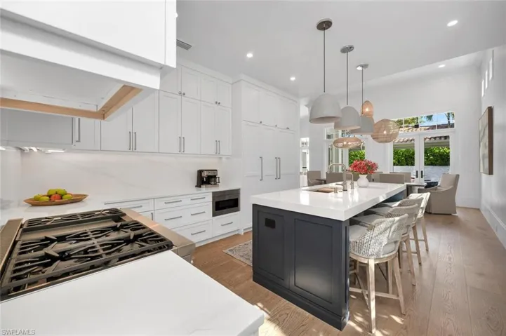 Kitchen featuring hanging light fixtures, sink, an island with sink, white cabinetry, and light wood-type flooring