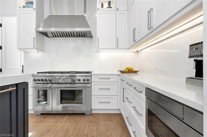 Kitchen featuring white cabinets, stainless steel appliances, wall chimney exhaust hood, and light wood-type flooring