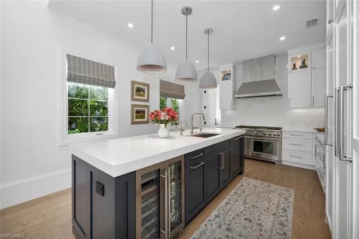 Kitchen with white cabinetry, stainless steel stove, an island with sink, and hanging light fixtures