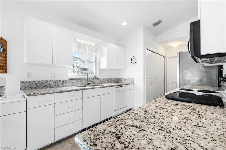 Kitchen with dishwasher, a sink, white cabinetry, light stone countertops, and recessed lighting