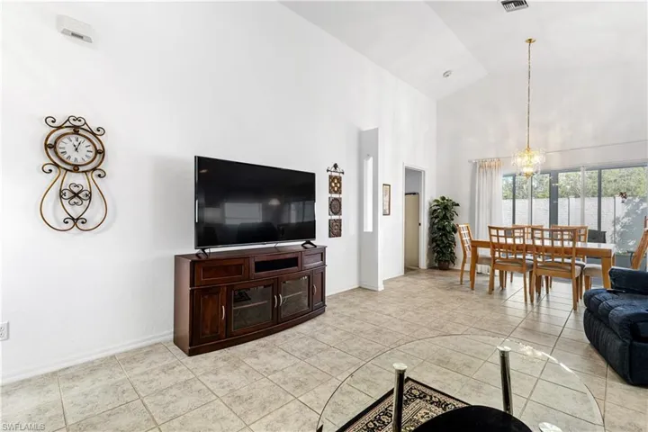 Living area with high vaulted ceiling, a chandelier, baseboards, and light tile patterned floors