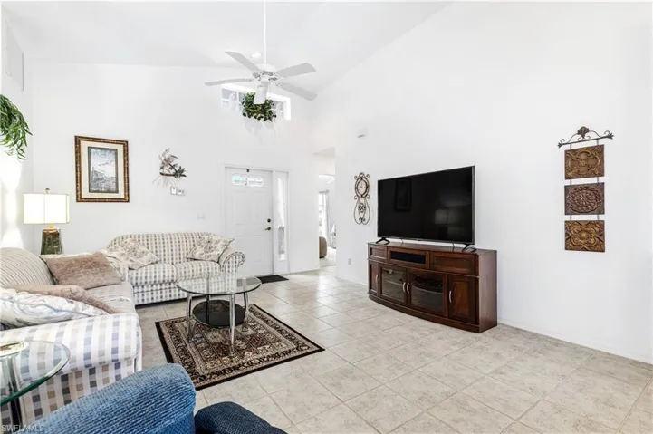 Living room with tile patterned floors, a ceiling fan, high vaulted ceiling, and baseboards