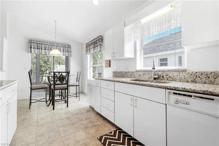 Kitchen with dishwasher, a sink, white cabinetry, lofted ceiling, and light stone countertops