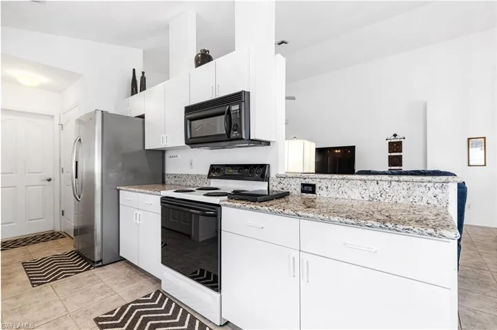 Kitchen featuring black microwave, electric range, a peninsula, freestanding refrigerator, and white cabinets