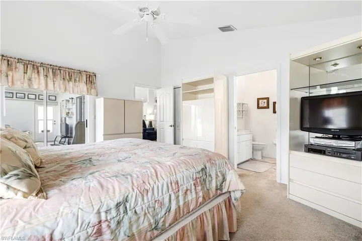 Bedroom with light colored carpet, connected bathroom, and high vaulted ceiling