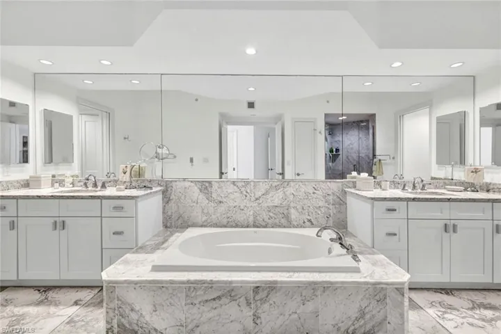 Bathroom featuring recessed lighting, two vanities, a bath, and marble finish floors